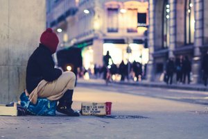 INTERACT Frau sitzt auf einer Tasche auf dem Boden in einer Straße